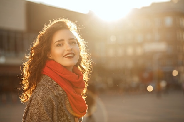 Portrait de mode de vie du modèle brune joyeuse avec des lèvres rouges marchant dans la rue en soirée ensoleillée. Espace pour le texte
