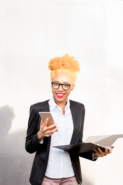 Portrait de mode de vie d'une femme d'affaires africaine en costume décontracté utilisant un téléphone sur fond de mur gris