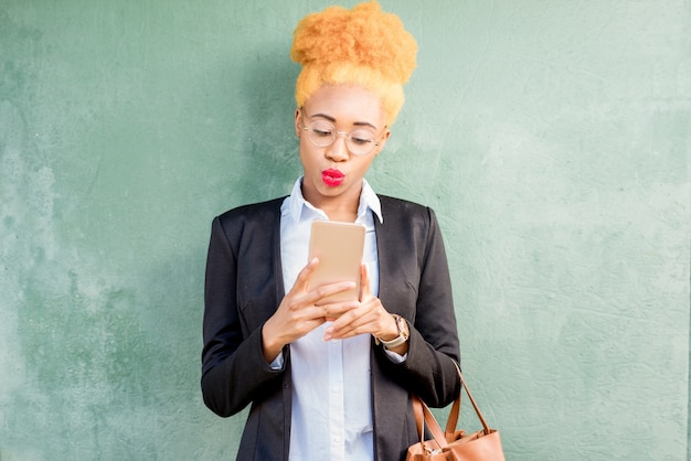 Portrait de mode de vie d'une femme d'affaires africaine en costume décontracté utilisant un téléphone intelligent sur fond de mur vert