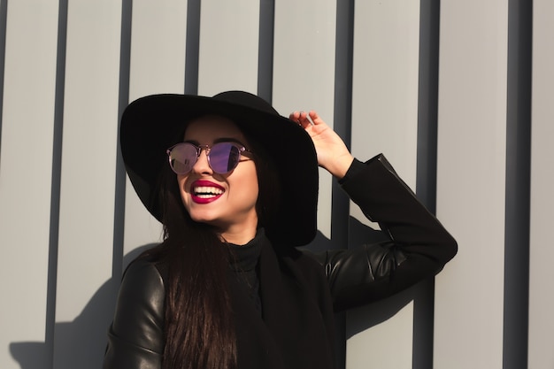 Portrait de mode de vie d'une femme brune heureuse dans un chapeau à large bord tendance et des lunettes élégantes posant à la lumière du soleil