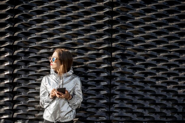 Portrait de mode de vie d'une femme élégante en veste argentée debout sur le fond de mur noir moderne