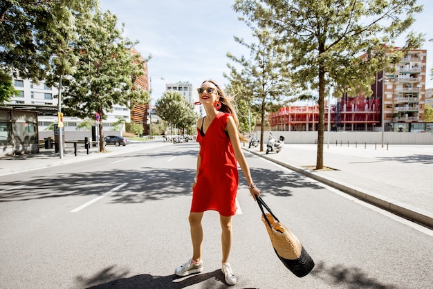 Portrait de mode de vie d'une femme en robe rouge traversant la rue dans le quartier moderne de la ville de Barcelone