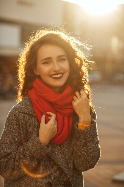 Portrait de mode de vie d'une femme souriante riante aux cheveux ondulés portant un manteau gris et une écharpe rouge