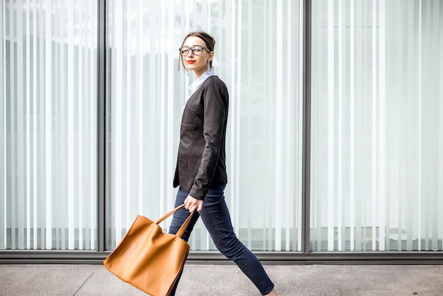 Portrait de mode de vie d'une jeune femme d'affaires marchant à l'extérieur avec un sac sur le fond du mur du bureau