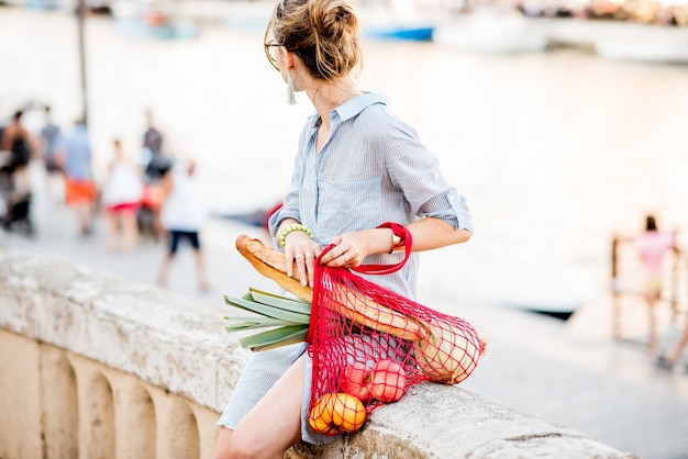 Portrait de mode de vie d'une jeune femme avec un sac en filet plein de produits frais regardant en arrière dans la vieille ville