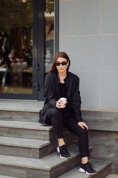 Portrait de mode de vie en plein air d'une superbe fille brune. Boire du café et marcher dans la rue de la ville.