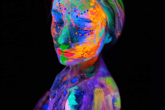 Portrait d'un modèle avec du maquillage fluorescent posant à la lumière UV avec du maquillage coloré