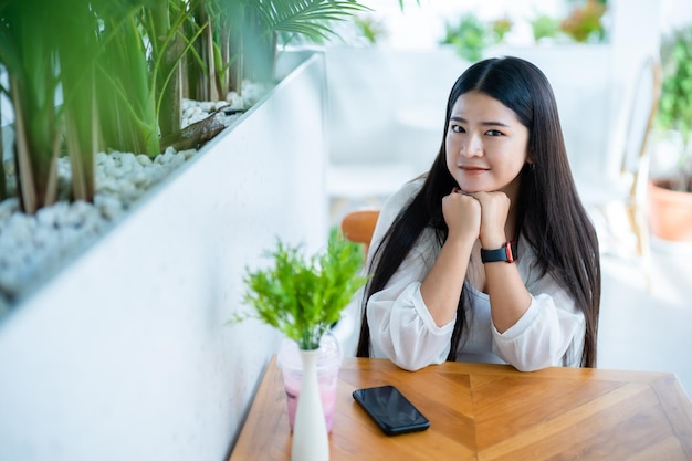 Portrait moderne d'une belle voyageuse asiatique heureuse portant une montre intelligente vêtue d'une belle robe blanche et portant un style de vie en jeans profitant d'un fond de restaurant de café assis