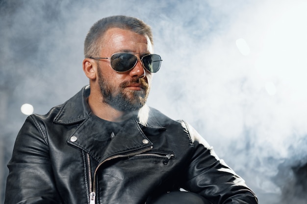 Portrait de motocycliste homme barbu en lunettes de soleil sombres sur fond sombre