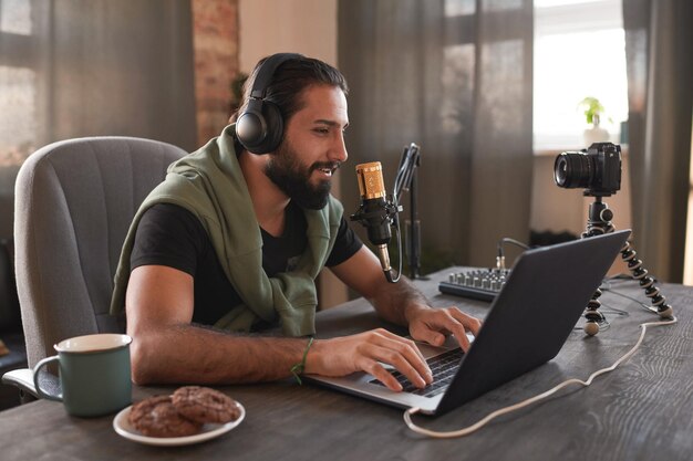 Photo portrait moyen horizontal d'un beau jeune homme barbu du moyen-orient assis seul dans un loft créant du contenu pour son blog