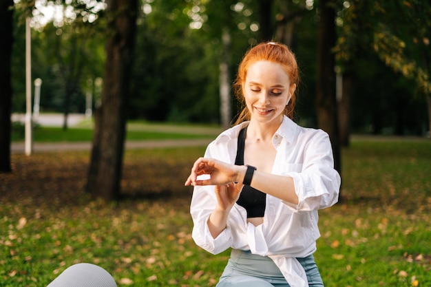 Portrait moyen d'une jeune femme assise sur un banc à l'aide d'une montre intelligente reposant dans le parc de la ville à l'extérieur Coureuse vérifiant le moniteur de fréquence cardiaque avant de faire du jogging