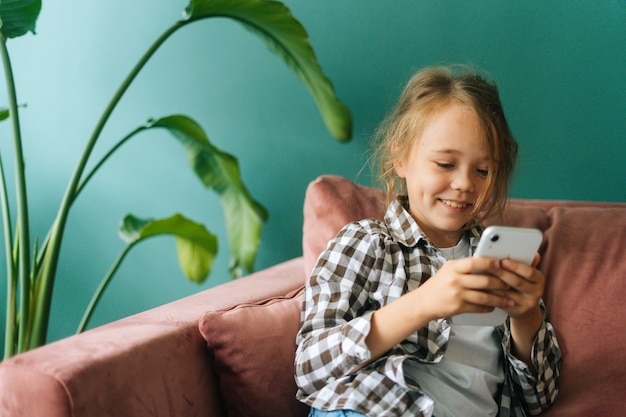 Portrait moyen d'une petite fille mignonne et joyeuse utilisant un smartphone en regardant l'écran en train de regarder