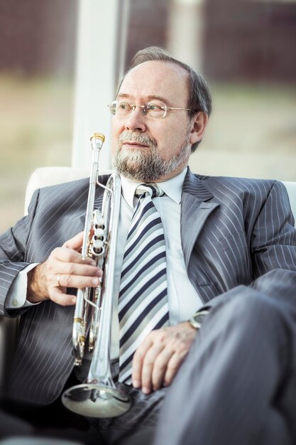 Portrait d'un musicien avec une trompette assis sur une chaise sur le fond de la salle de concert