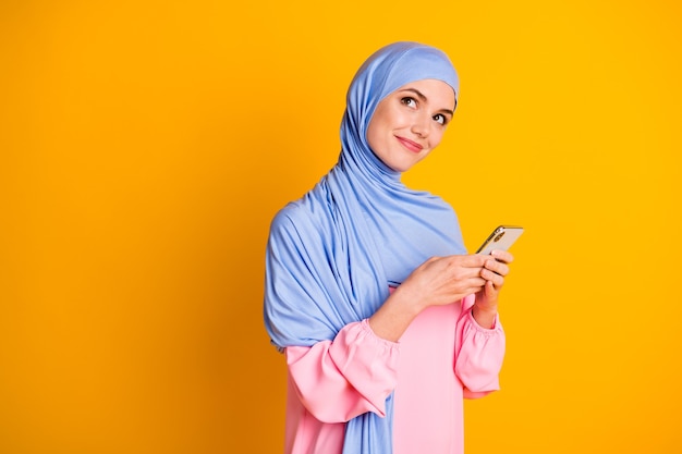 Portrait De Muslimah Rêveur Créatif Assez Joyeux Utilisant L'application De L'appareil 5g Créant Un Poste Isolé Sur Fond De Couleur Jaune Vif