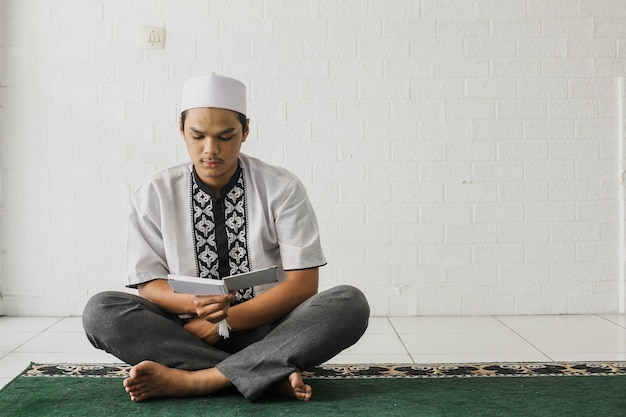 Portrait d'un musulman religieux portant une chemise koko lisant le Coran sérieusement dans la mosquée