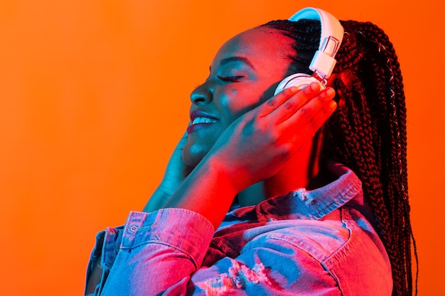 Portrait de néon de jeune femme africaine écoutant de la musique avec des écouteurs.