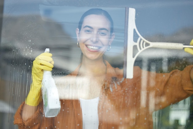 Portrait de nettoyage de vitres sourire et femme heureuse à la maison laver les vitres avec un nettoyant pour vitres Aider le travail et la femme de ménage avec un produit détergent en aérosol pour les tâches ménagères et un chiffon désinfectant avec une raclette