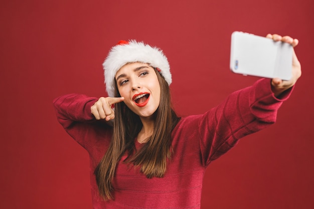 Portrait de Noël de belle fille portant un chapeau de père Noël, souriant et faisant selfie sur téléphone mobile