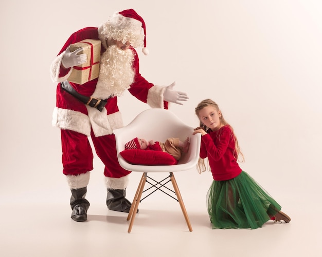 Portrait de Noël d'une jolie petite fille nouveau-née, d'une jolie soeur adolescente, vêtue de vêtements de Noël et d'un homme portant un costume et un chapeau de père Noël, tourné en studio, heure d'hiver. Le noël, concept de vacances