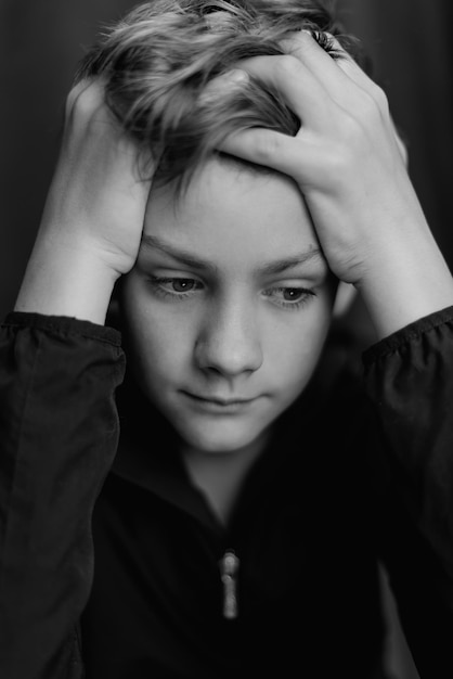 Portrait noir et blanc d'un adolescent sur fond sombre Gros plan discret d'un jeune garçon adolescent Photographie noir et blanc Mise au point sélective