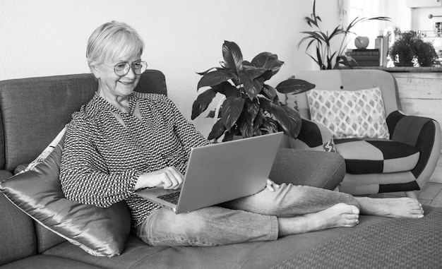 Portrait noir et blanc d'une femme mûre se reposant sur un canapé à la maison tout en utilisant un ordinateur portable