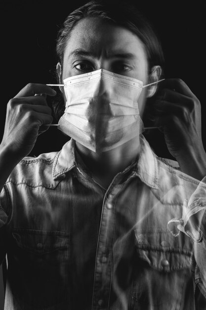 Portrait noir et blanc d'un homme latin mettant un masque médical sur fond noir