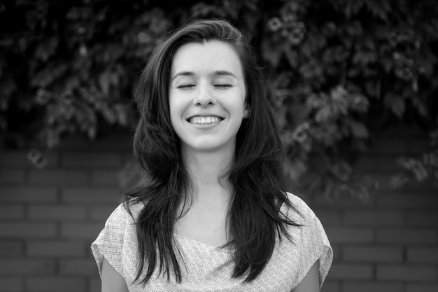 Portrait noir et blanc de jeune brune, femme, souriant sincèrement, les yeux fermés