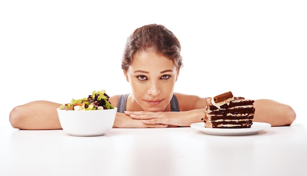 Photo portrait de nourriture et choix avec une femme en studio sur fond blanc pour décider entre une salade ou un gâteau régime alimentaire ou santé avec un dessert au chocolat et un bol sain de légumes frais