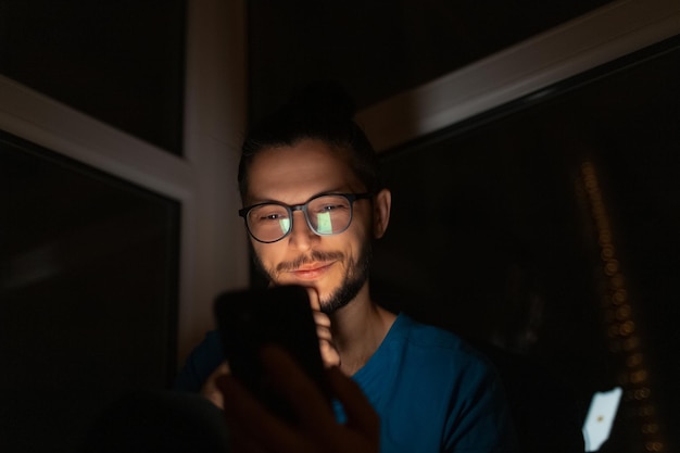 Portrait de nuit d'un jeune homme souriant avec un smartphone à la main