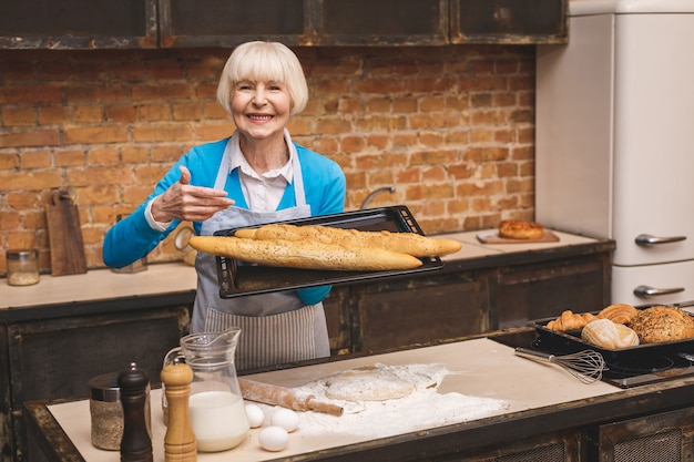 Portrait of attractive smiling happy senior age woman is cooking on kitchen. Grand-mère faisant une pâtisserie savoureuse.