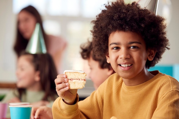 Portrait Of Boy Eating Birthday Cake At Party avec parents et amis à la maison