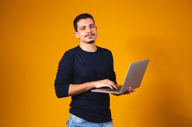 Portrait of boy holding laptop travaillant dans les mains isolées sur fond jaune.