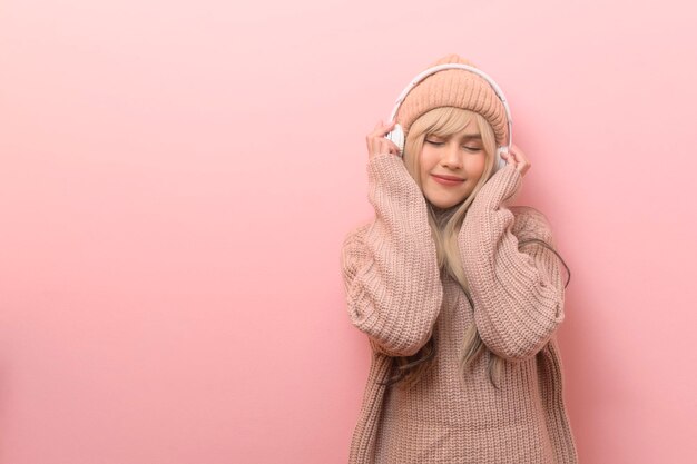 Portrait of Caucasian young woman wearing sweater à l'aide d'écouteurs sur fond rose