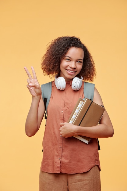 Portrait of cheerful cool étudiante afro-américaine en chemise sans manches montrant deux doigts sur fond jaune