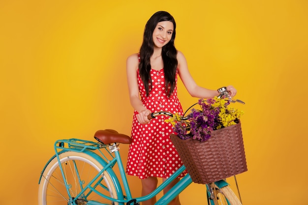 Portrait of courier lady ride bike livrer des fleurs porter une mini robe rouge pointillée sur fond jaune