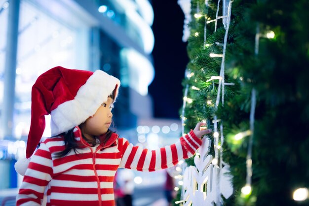 Portrait of cute asian little girl wear santa hat happy near christmas treeThailand kid rejoignez le festival de noël