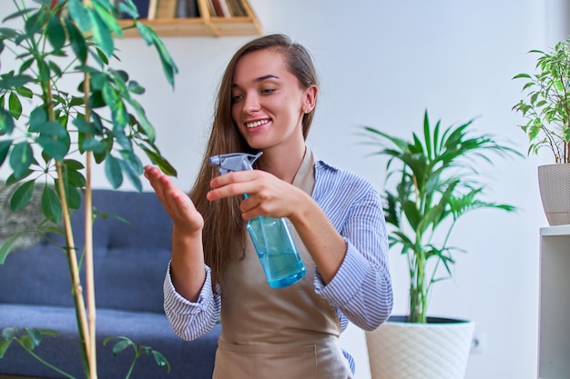 Portrait of cute happy young smiling jolie femme jardinier en tablier d'arrosage des plantes d'intérieur à l'aide de vaporisateur