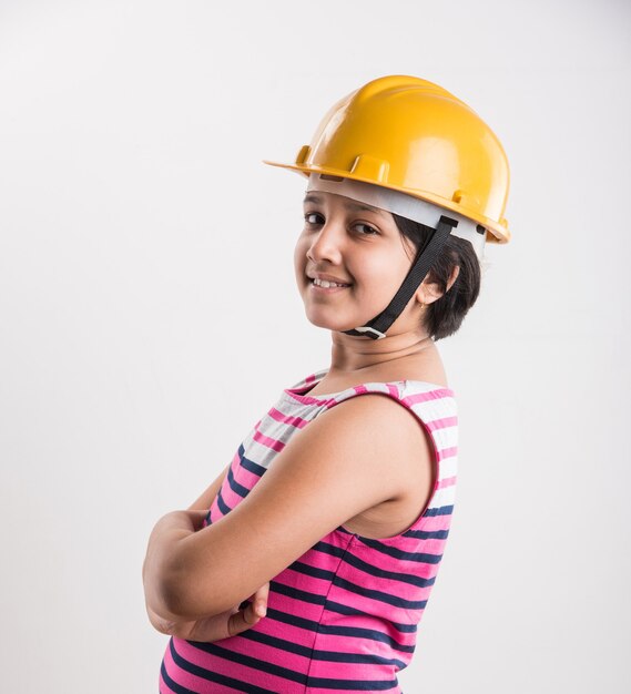 Portrait of cute little Indian girl in yellow hard hat holding paper roll, debout isolé sur fond blanc