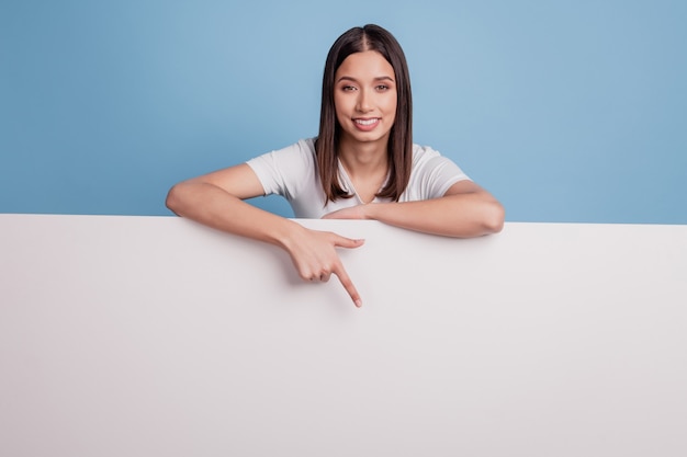 Portrait of cute promoteur conseiller dame doigt direct vers le bas panneau d'affichage mur blanc espace vide sur fond bleu