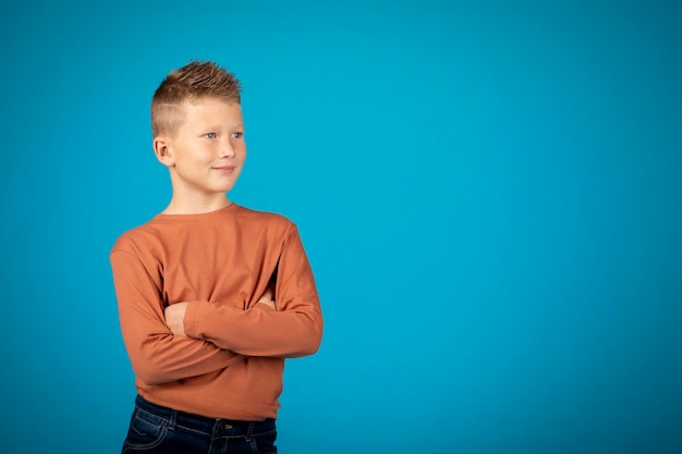 Portrait Of Handsome Preteen Boy avec les bras croisés debout sur fond bleu