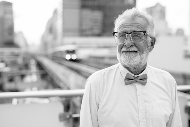 Portrait of handsome senior tourist man portant des vêtements élégants tout en explorant la ville de Bangkok en noir et blanc