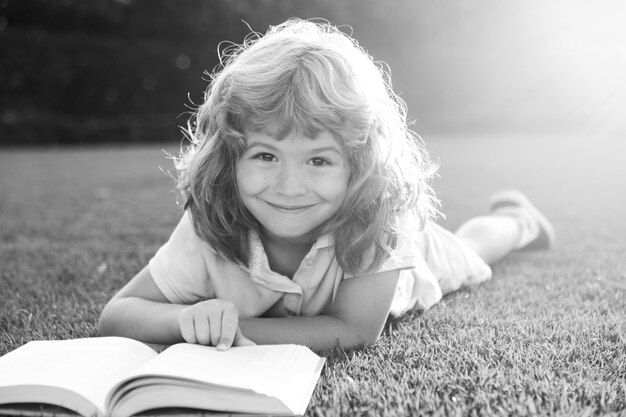 Portrait of happy child boy with book in park Kids early education Little kid lire un livre dans la garde