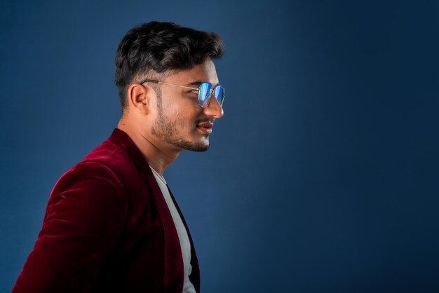 Portrait of Happy Indian jeune homme portant un blazer avec des lunettes posant sur un fond bleu