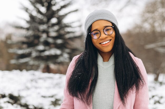 Portrait of happy positive girl African American young woman in glasses and gloves in winter park