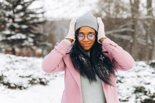 Portrait of happy positive girl African American young woman in glasses and gloves in winter park