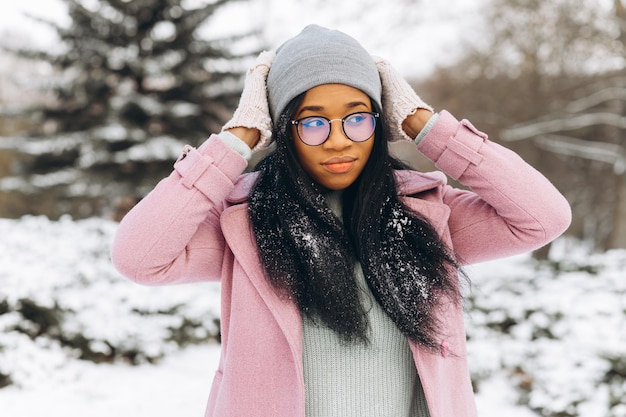 Portrait of happy positive girl African American young woman in glasses and gloves in winter park