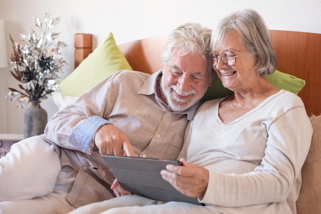 Portrait of happy senior couple ensemble au lit des personnes âgées se détendre à la maison à l'aide de tablette numérique