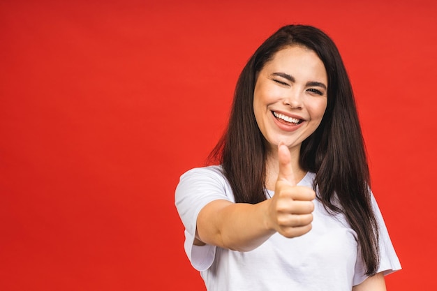 Portrait of happy smiling brunette business girl woman in casual isolé sur fond rouge Thumbs up