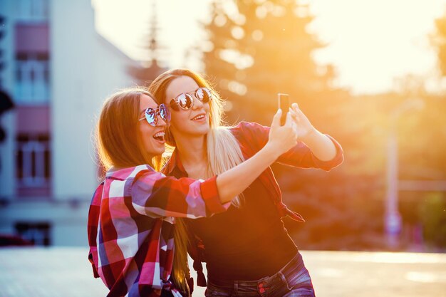 Portrait of a happy two smiling girls making selfie photo sur fond urbain smartphone le soir