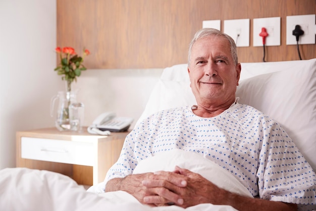 Portrait of male senior patient allongé dans son lit d'hôpital souriant à la caméra